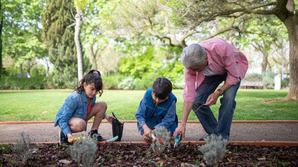 two young kids gardening with an older man in pink shirt