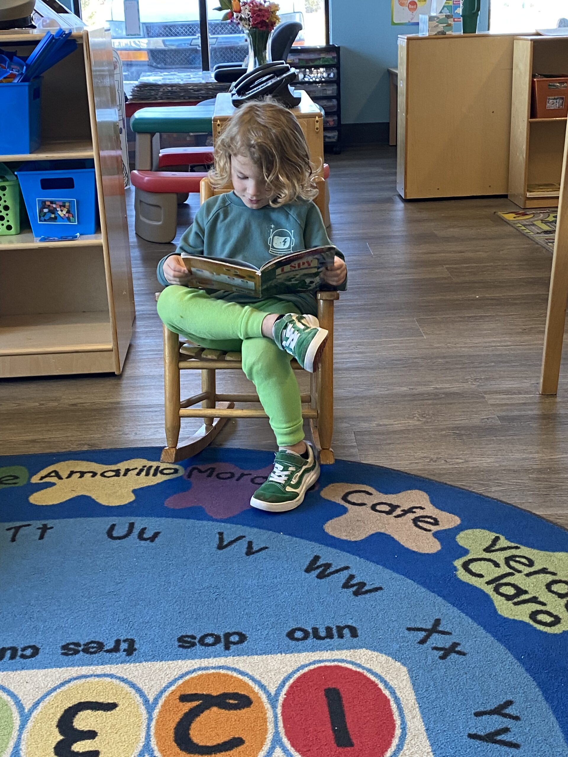 A kid reading a book while seated in a chair